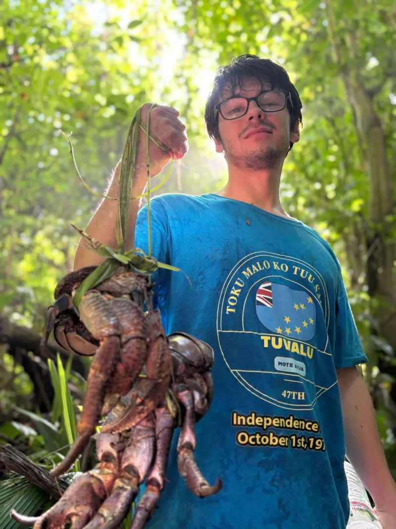 Nick Miller holding a coconut crab on a Tuvaluan beach.
